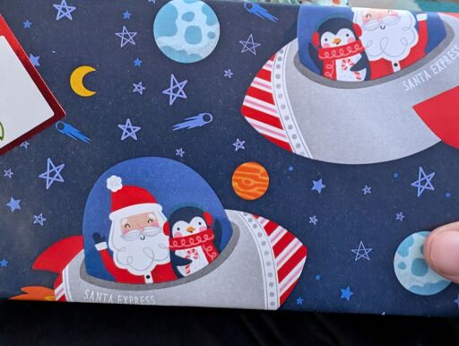 Christmas gift wrapped in paper showing santa and a penguin in a space ship.